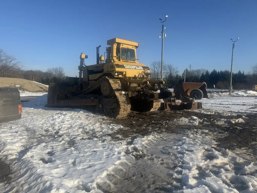 Yellow bulldozer sitting in snow on a cold, sunny day before repair work