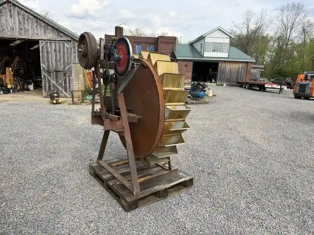Large industrial wheel on a stand in the yard beside the shop's buildings