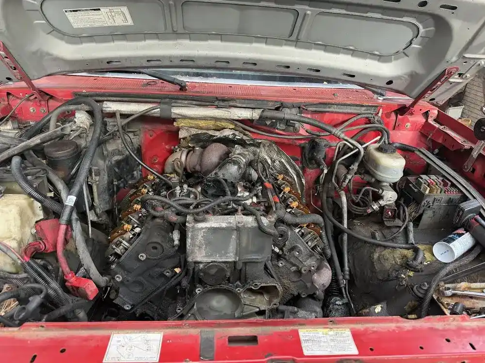 Red truck engine bay with the engine half rebuilt and wiring hanging loose