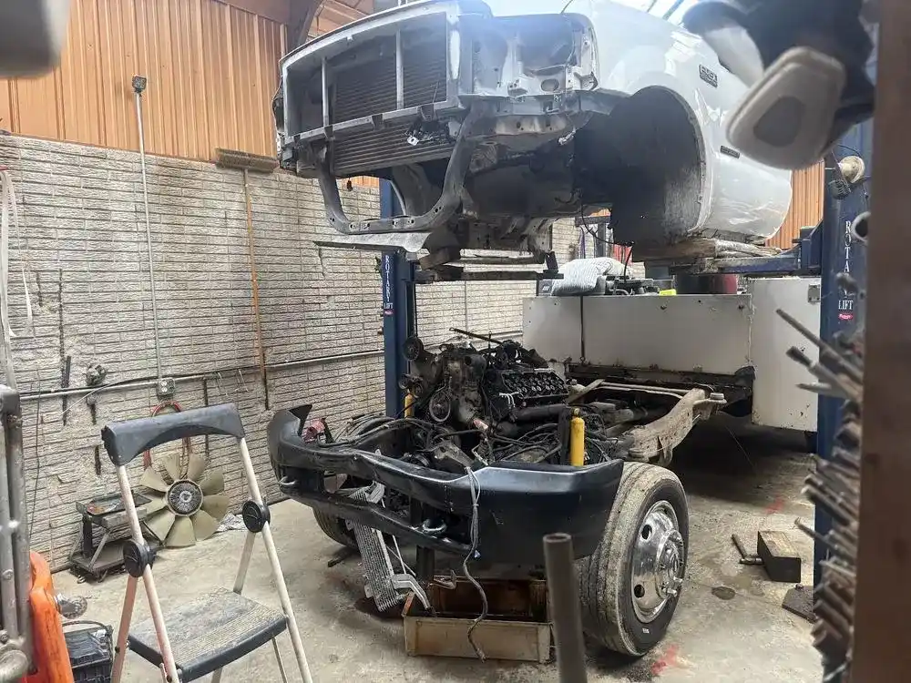 White truck on a lift with its engine pulled down onto the chassis in the shop